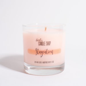 May include: A clear glass candle jar with a pink soy wax candle inside. The candle has a label that reads "Anel's Candle Shop Staycation Soy Wax Blend | Handpoured in NY | 9.2 oz."