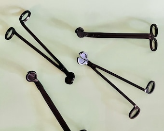May include: Four black metal candle wick trimmers with different handle designs. The trimmers are used to trim candle wicks.