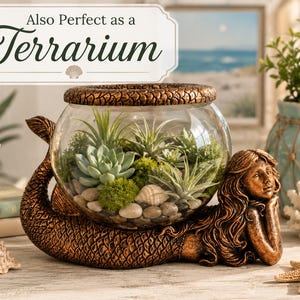 May include: A bronze-colored mermaid-shaped terrarium base supports a clear glass bowl filled with succulents, moss, and small stones. The text "Also Perfect as a Terrarium" is displayed above the terrarium. Seashells and a starfish are placed near the base.