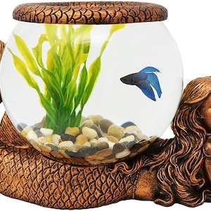 May include: A bronze-colored mermaid-shaped aquarium. The fishbowl is held by the mermaid's tail and arms. Inside the bowl are small pebbles, green plants, and a blue betta fish. The top of the bowl has a decorative, textured rim.