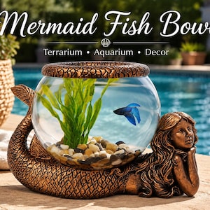 May include: A mermaid-shaped fish bowl with the text "Mermaid Fish Bowl". The bronze-colored bowl holds a blue fish, green plants, and small stones. The mermaid is lying down, supporting the bowl with her tail and arms.