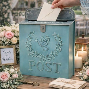 May include: A teal wedding card box with a dove and floral design, with the word "POST" embossed on the front. A hand is placing a card into the slot. The words "Cards & Wishes" are in a framed sign. The words "Wedding Card Box" are at the bottom.