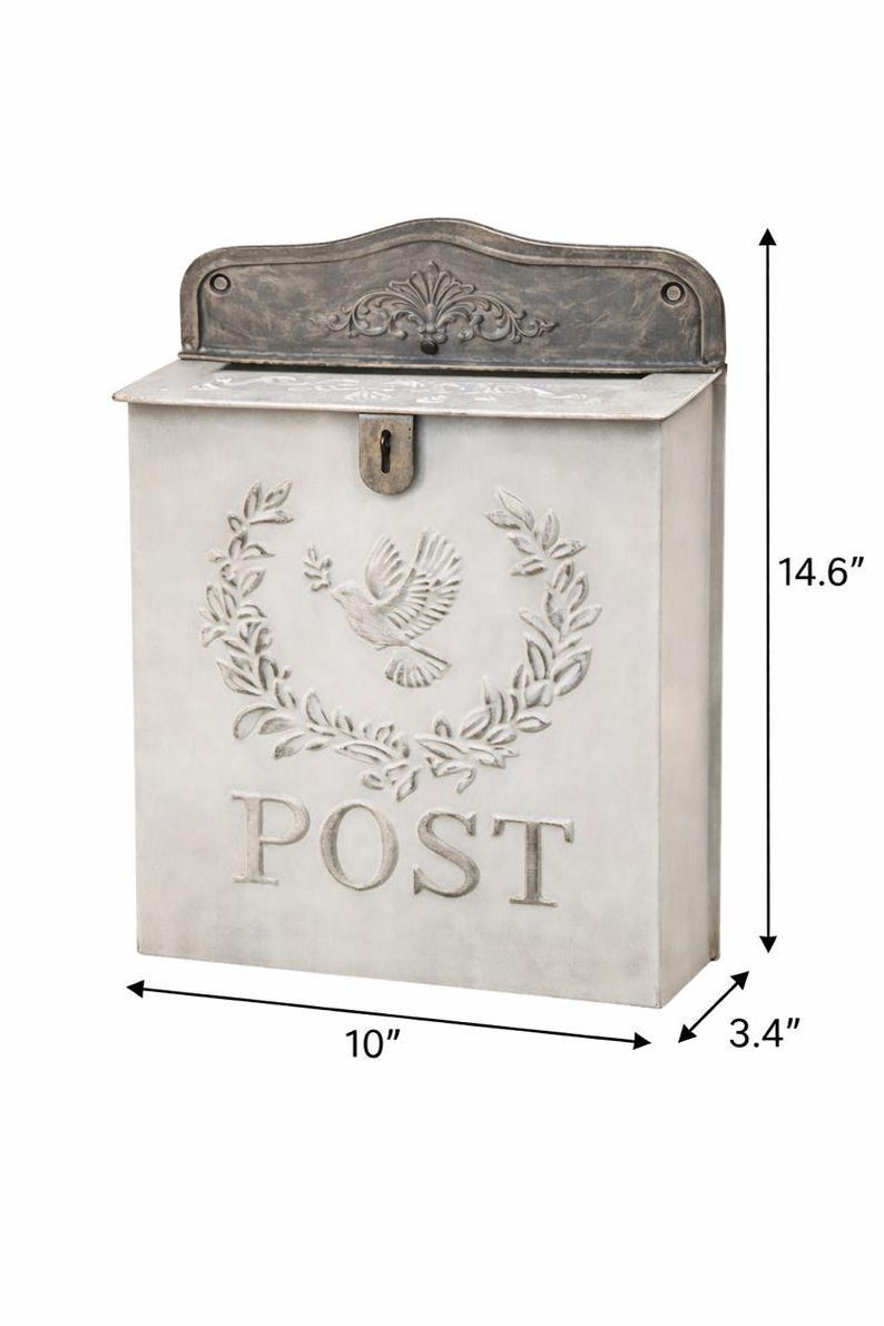 May include: A rectangular, off-white metal mailbox with a decorative top and a keyhole. The front features a dove and wreath design, with the word "POST" below. It measures 10 inches wide, 3.4 inches deep, and 14.6 inches tall.