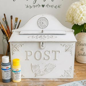 May include: A white vintage mailbox with the word "POST" in raised letters and a bird design. The mailbox has decorative scrollwork and is accompanied by paint bottles, brushes, and stencils. The text "PAINT YOUR OWN Vintage Mailbox" is at the top.