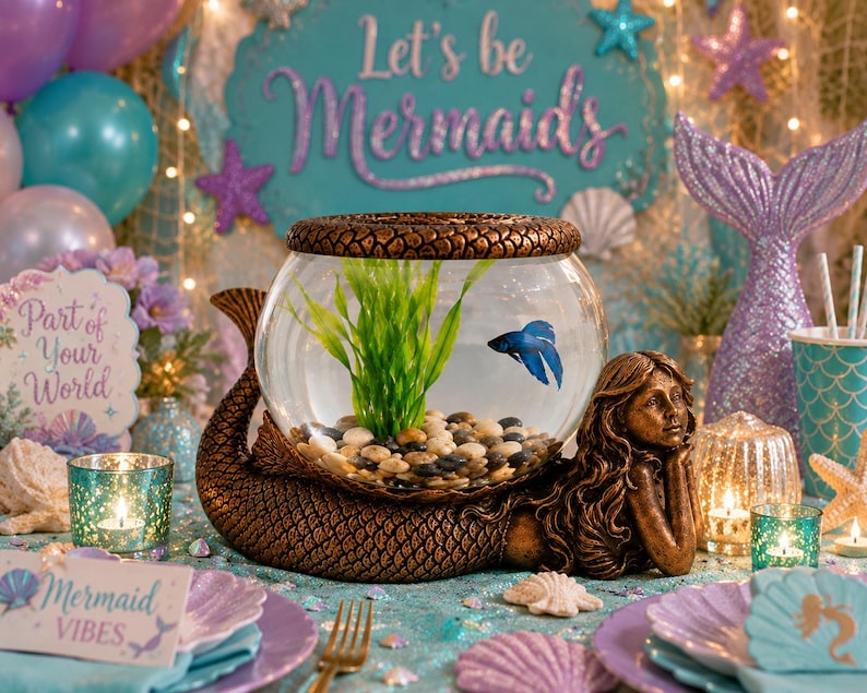 May include: A mermaid-themed centerpiece features a fishbowl with a blue betta fish, resting on a bronze mermaid sculpture. The scene includes a sign that says "Let's be Mermaids", seashells, and teal and purple accents, creating a whimsical underwater vibe.