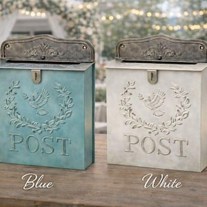 May include: Two decorative metal mailboxes, one blue and one white, with a vintage design. Each mailbox features a dove and laurel wreath motif, the word "POST", and a decorative lid. The blue mailbox is labeled "Blue", and the white mailbox is labeled "White".