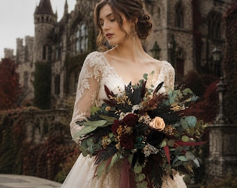 May include: A long-sleeved lace gown with a V-neckline paired with a large, dark-toned floral bouquet featuring deep red roses, black foliage, eucalyptus leaves, and dried elements, accented by long, flowing burgundy ribbons tied at the stems.