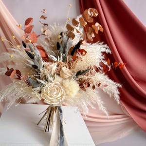 Boho wedding bouquet made with dried flowers, featuring a custom handmade bridal bouquet and coordinating bridesmaids bunches. Everlasting floral arrangements in soft natural tones, perfect as timeless bridal accessories for a rustic or bohemian wedding celebration.