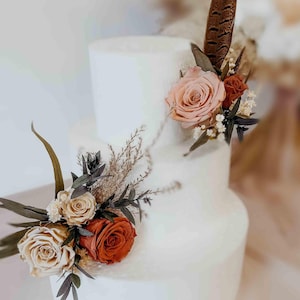 Terracotta and ivory dried flower wedding cake toppers with preserved roses, hydrangea, bunny tails, oats and limonium arranged on a modern white wedding cake. Neutral boho cake flowers for rustic, Italian countryside and earth tone weddings. Natural preserved floral cake decor handmade for bridal shower, wedding reception or engagement party.