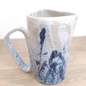 Puede incluir: Una jarra de cerámica blanca con un diseño de salpicaduras azul y blanco. La jarra tiene un asa y una boca ancha.