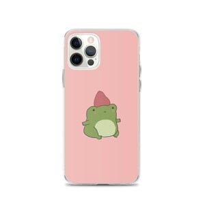 May include: A clear phone case featuring a cartoon frog wearing a strawberry hat. The frog is green with a white belly and is centered on a pink background. The phone case has a glossy finish.