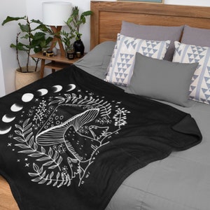 May include: Black fleece throw blanket with a white design of a mushroom with a crescent moon and stars. The blanket is on a bed with pillows.