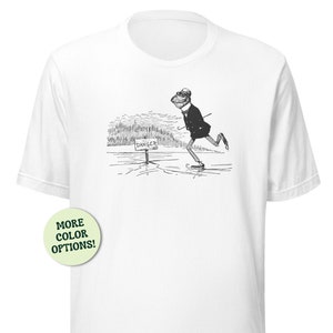 May include: White t-shirt with a black and white illustration of a frog wearing a suit and ice skating on a frozen lake. The frog is skating past a sign that reads "Danger".