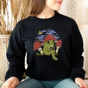 Süßes Frosch Pilz Hut Lesebuch Unisex Sweatshirt, Goblincore Kröte mit Roman, Schnecke und Toadstool, Happy Cottagecore Bookish Unter Mond