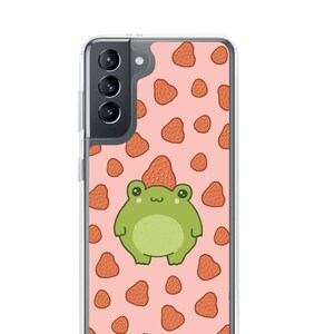May include: A clear phone case with a pink background and a pattern of red strawberries. A green frog with a strawberry on its head is in the center of the case.