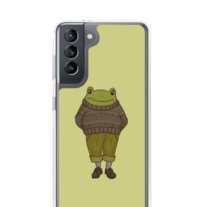 May include: A green frog wearing a brown and white patterned sweater and brown pants. The frog is standing on a light green background. The image is on a clear phone case.