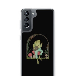 May include: A black phone case with a clear back and a green frog playing a banjo in a woodland setting. The frog is sitting on a mushroom and surrounded by other mushrooms and foliage.