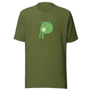May include: A green t-shirt with a cartoon frog holding a flower. The frog has a happy expression and is sitting on its hind legs.