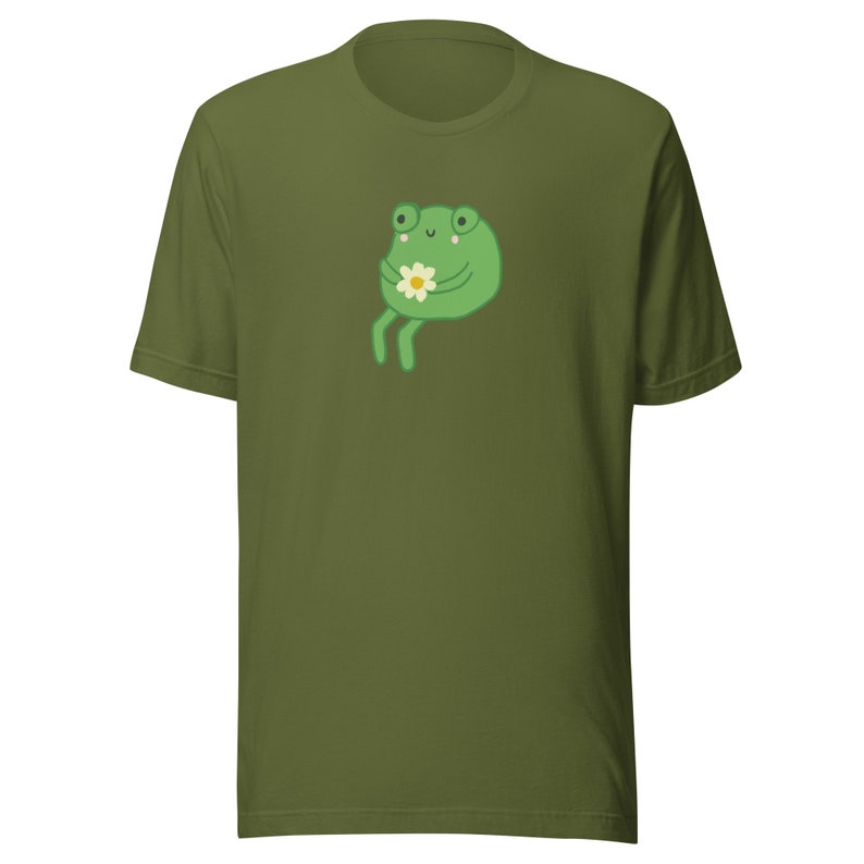 May include: A green t-shirt with a cartoon frog holding a flower. The frog has a happy expression and is sitting on its hind legs.