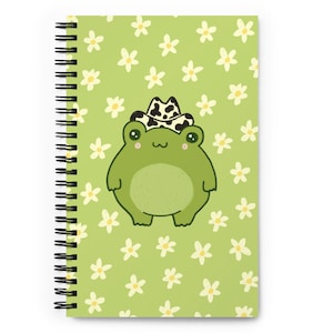 May include: A spiral-bound notebook featuring a cartoon frog wearing a cow-print cowboy hat. The frog is green with large eyes and a light green belly. The notebook has a light green background with white daisy flowers.