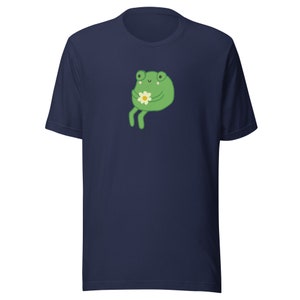 May include: A navy blue t-shirt with a green frog holding a white flower. The frog has a happy expression on its face.