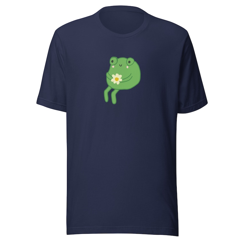May include: A navy blue t-shirt with a green frog holding a white flower. The frog has a happy expression on its face.