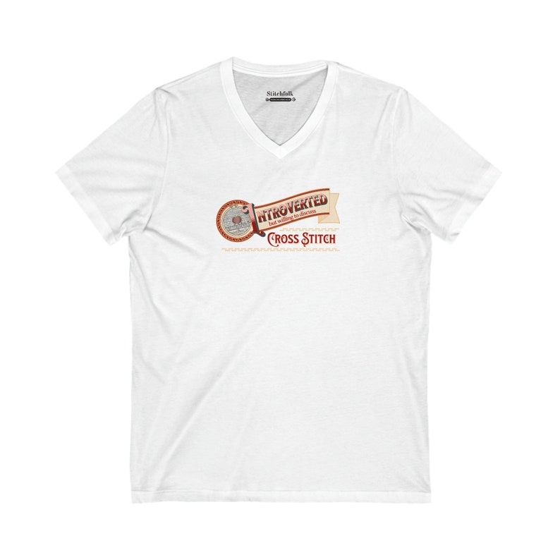 Op de afbeelding: Wit V-hals T-shirt met een afbeelding met de tekst "Introvert maar bereid om kruissteken te bespreken". Het ontwerp heeft een cirkelvormig embleem en een banner in bruin- en roodtinten. Het shirt is gemaakt van een zacht, comfortabel materiaal.