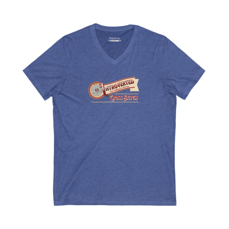 Op de afbeelding: Blauw V-hals T-shirt met de tekst "Introvert maar bereid om kruissteek te bespreken". Het ontwerp bevat een banner en een cirkelvormig embleem met kruissteekdetails. Het shirt is gemaakt van een zacht, comfortabel materiaal.