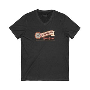 Op de afbeelding: Donkergrijs V-hals T-shirt met de tekst "Introverted but willing to discuss Cross Stitch" in een vintage design. De afbeelding bevat een cirkelvormig element met naald en draad, en een banner met het woord "Introverted".
