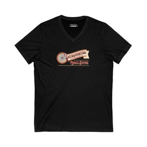 Op de afbeelding: Zwart V-hals T-shirt met de tekst "Introvert maar bereid om kruissteek te bespreken". Het ontwerp bevat een banner en een illustratie van een borduurring.