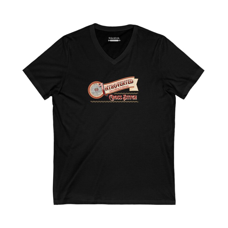 Op de afbeelding: Zwart V-hals T-shirt met de tekst "Introvert maar bereid om kruissteek te bespreken". Het ontwerp bevat een banner en een illustratie van een borduurring.