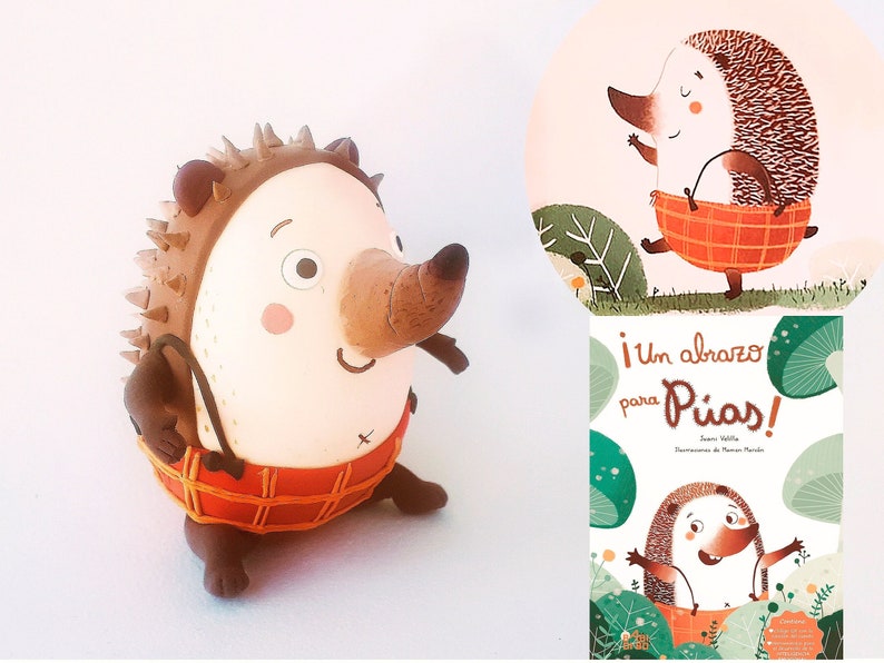 May include: A brown and white hedgehog figurine with a red and orange plaid skirt. The figurine is holding a brown basket. The image also shows a book cover with a similar hedgehog illustration and the text "&iexcl;Un abrazo para P&iacute;as!"