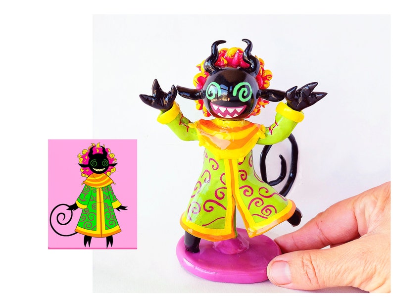 May include: A hand-painted figurine of a black demon with green and yellow clothing. The demon has pink and orange curly hair and a long black tail. The figurine is standing on a pink base.