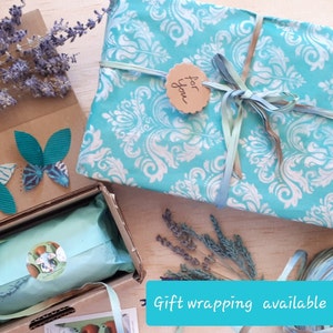 May include: A turquoise gift box with a white damask pattern is wrapped with a turquoise ribbon and a brown tag that says "for you". The box is sitting on a wooden surface with lavender sprigs and a brown cardboard box with butterfly cutouts.