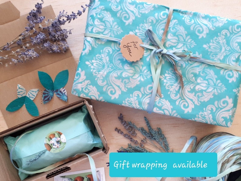 May include: A turquoise gift box with a white damask pattern is wrapped with a turquoise ribbon and a brown tag that says "for you". The box is sitting on a wooden surface with lavender sprigs and a brown cardboard box with butterfly cutouts.
