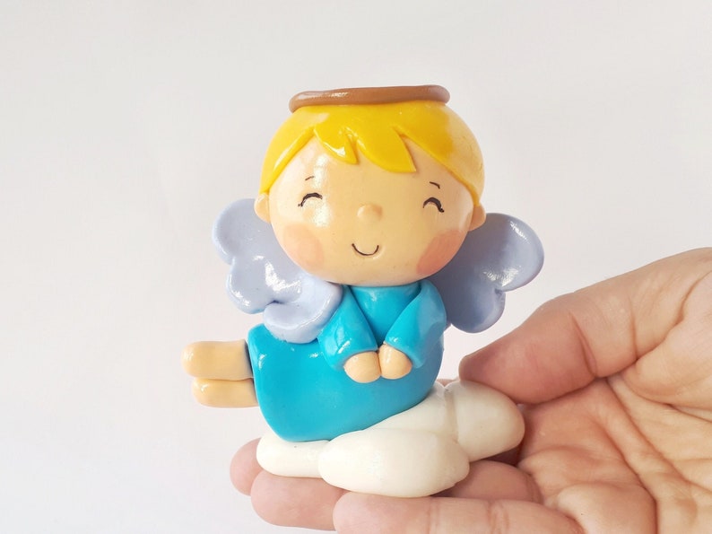 May include: A small, blue angel figurine with a halo, yellow hair, and wings. The angel is sitting on a white cloud.