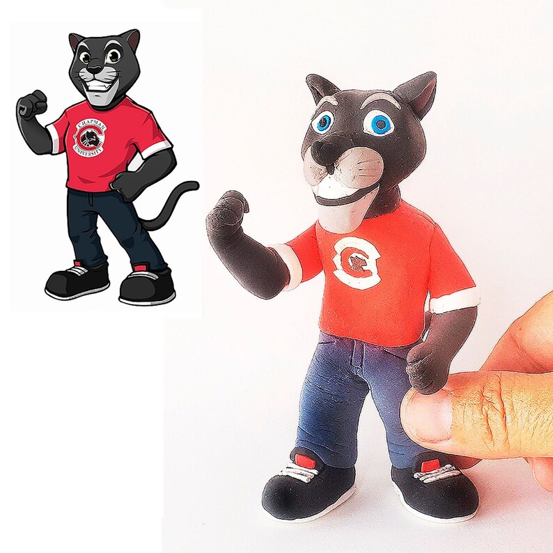 May include: A black and grey cartoon panther mascot wearing a red shirt with the text "Chapman University" and blue jeans. The mascot is standing with its arms by its side and its tail curled around its legs.