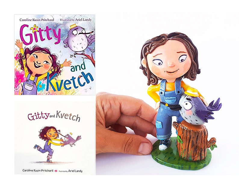 May include: A handmade figurine of a girl with brown hair wearing a yellow shirt and blue overalls. She is standing next to a small bird with a yellow hat on a tree stump. The figurine is based on the children's book "Gitty and Kvetch" by Caroline Kusin Pritchard, illustrated by Ariel Landy.