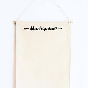 May include: A beige canvas banner with the text "Adventure Awaits" and an arrow pointing to the right. The banner is hanging from a white wall.