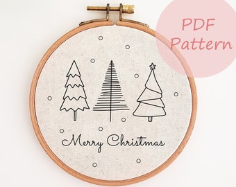 May include: A white embroidery hoop with a black line drawing of three Christmas trees and the text "Merry Christmas".