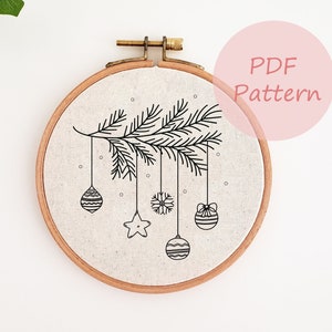 May include: A round embroidery hoop with a linen fabric featuring a black line drawing of a Christmas tree branch with ornaments. The ornaments include a snowflake, star, and striped and patterned baubles. The text "PDF Pattern" is in a pink circle.