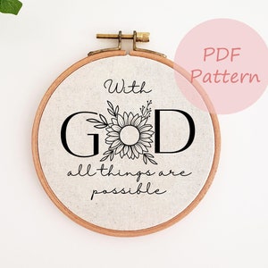 Op de afbeelding: Een witte borduurring met een zwart-wit ontwerp met de tekst "Met God is alles mogelijk". Het ontwerp bevat een gestileerde zonnebloem.