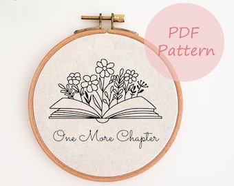 May include: A white embroidery hoop with a black line drawing of an open book with flowers growing out of it. The text "One More Chapter" is written below the book.
