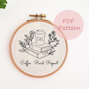 以下が含まれることがあります： コーヒーカップ、本、花の要素の黒い線画が描かれたリネンの生地が入った丸い刺繍枠。「Coffee. Read. Repeat」の文字が本の下にあります。「PDF Pattern」の文字はピンク色の円の中にあります。