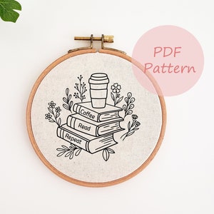 以下が含まれることがあります： コーヒーカップと「Coffee, Read, Repeat」と書かれた本の積み重ねを黒と白で刺繍したパターン。丸い布地に施されています。