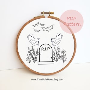May include: A Halloween-themed embroidery hoop featuring a black and white design. The design includes bats, ghosts, a tombstone with "R.I.P.", and floral elements. The hoop is made of wood and has a PDF pattern label.
