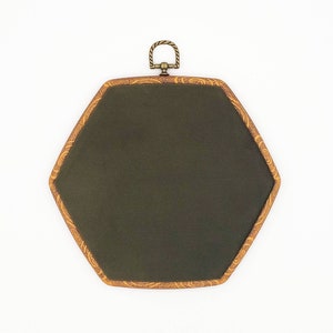 May include: A dark green, hexagonal wall hanging with a decorative gold-colored frame. The frame has a detailed, swirling pattern. A small, ornate metal loop is attached at the top for hanging. The background is white.
