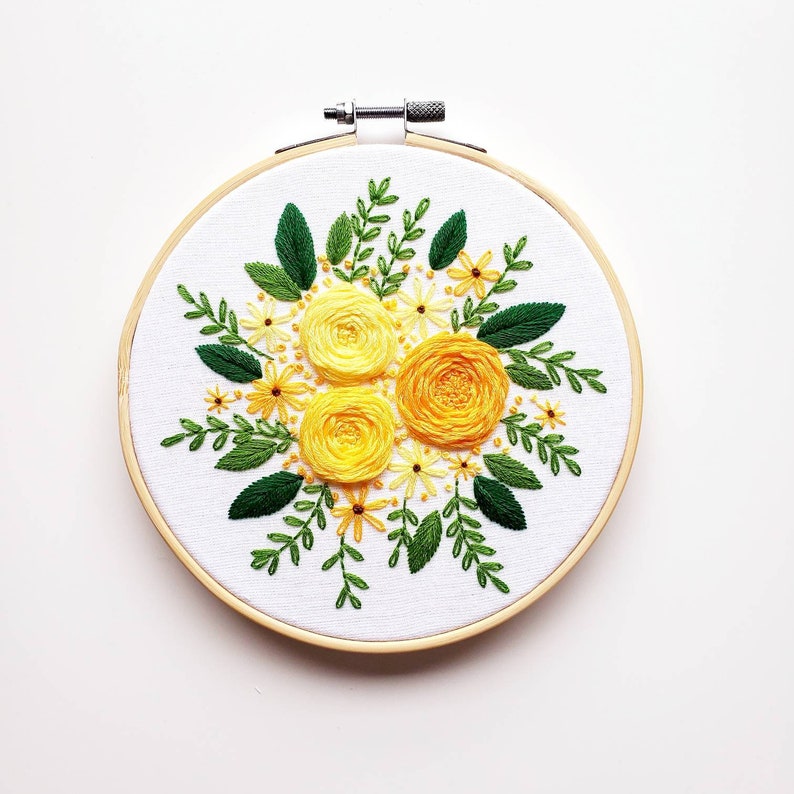 May include: Hand-stitched embroidery art featuring a vibrant floral design. The artwork showcases three large yellow roses surrounded by smaller yellow flowers and green leaves. The embroidery is set in a 6-inch wooden hoop, perfect for wall decor.