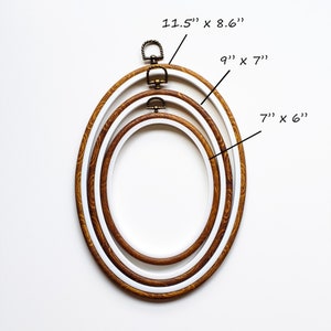 May include: Three oval embroidery hoops in varying sizes. The largest hoop measures 11.5" x 8.6", the middle one is 9" x 7", and the smallest is 7" x 6". Each hoop has a wooden outer ring and a white inner ring, with a metal clasp.