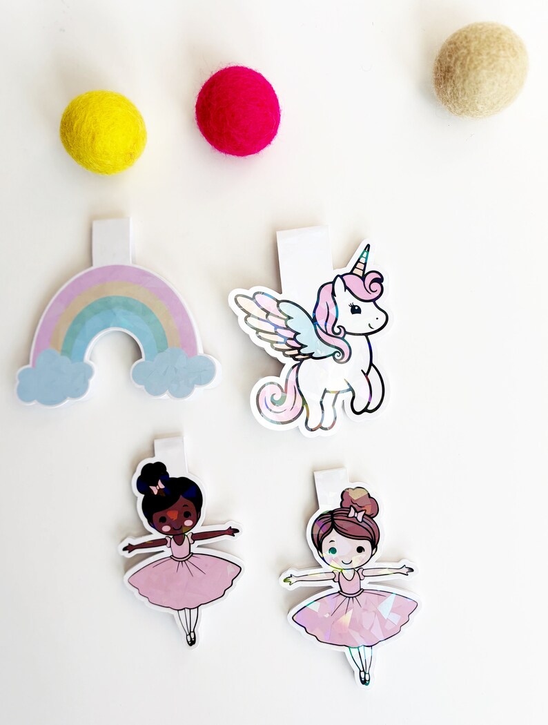 May include: Four colorful bookmarks with a rainbow, a unicorn, and two ballerinas. The bookmarks are made of iridescent paper and have a white backing.